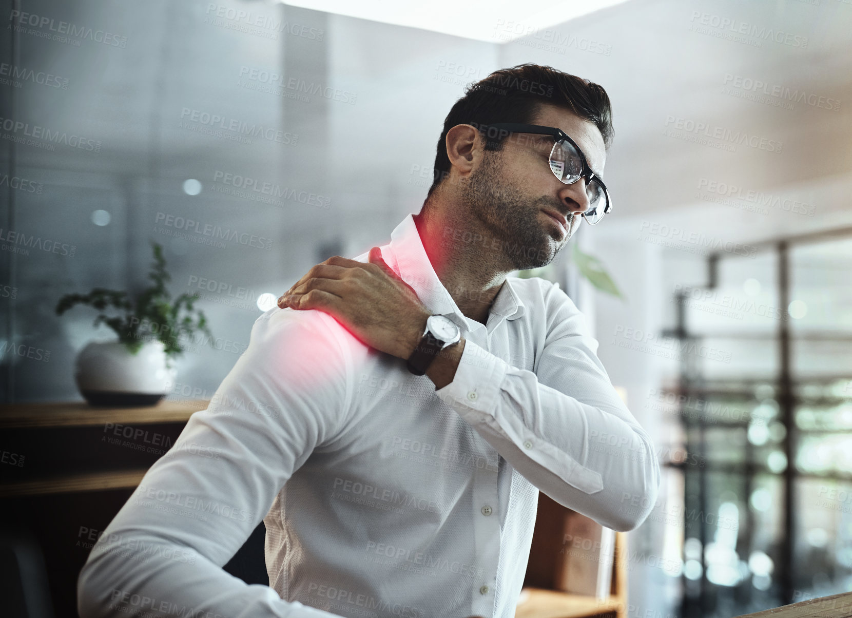Buy stock photo Shot of a young businessman suffering with shoulder pain while working in an office