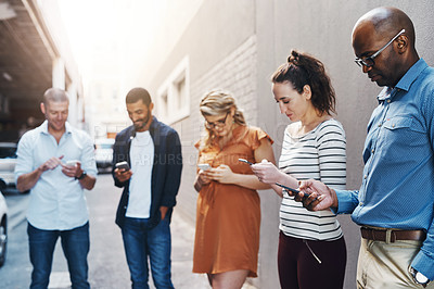 Buy stock photo Business people reading text on phone, checking notifications and typing messages online during a break at work. Group of diverse colleagues scrolling on the internet, browsing app and networking