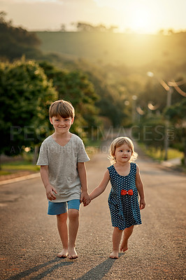 Buy stock photo Shot of an adorable little boy walking hand in hand with his sister down the road in the neighbourhood