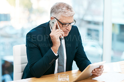Buy stock photo Cropped shot of a handsome mature businessman working on his tablet while making a phonecall in the office