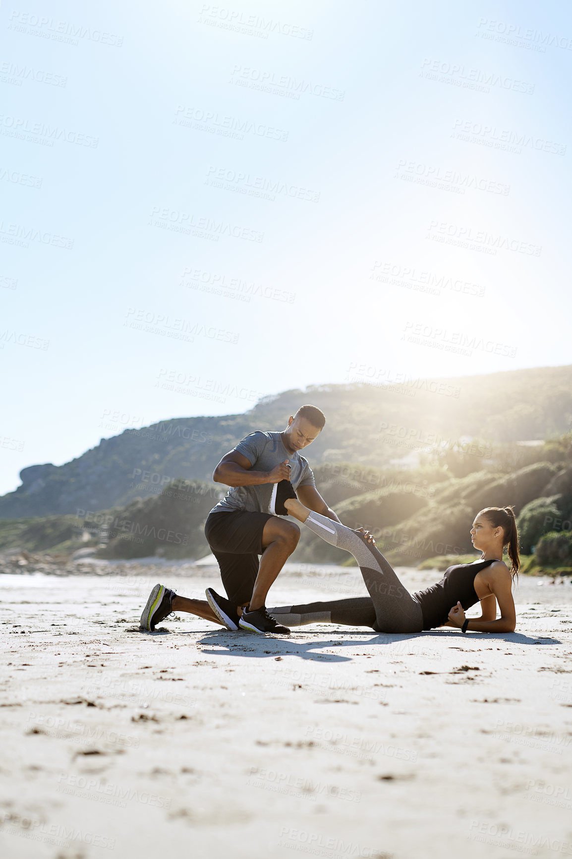 Buy stock photo Shot of a sporty young couple stretching while exercising along the beach