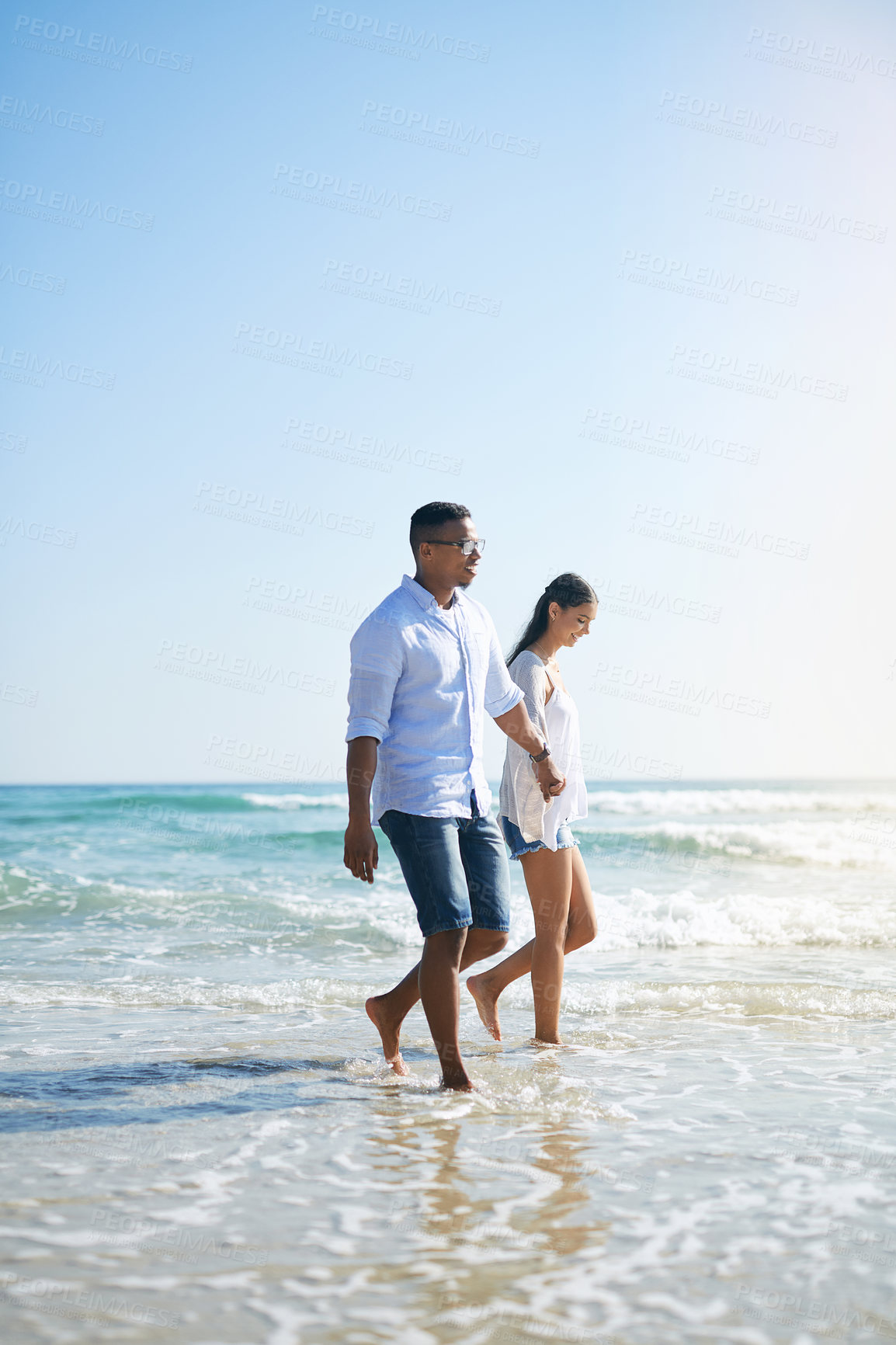 Buy stock photo Shot of a young couple taking a stroll along the beach