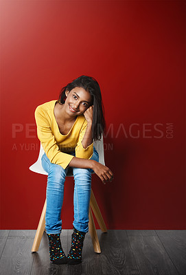 Buy stock photo Studio portrait of a beautiful young woman sitting on a chair against a red background