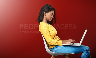 Buy stock photo Studio shot of an attractive young woman using a laptop against a red background