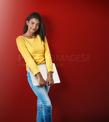 Buy stock photo Studio portrait of an attractive young woman holding a laptop against a red background