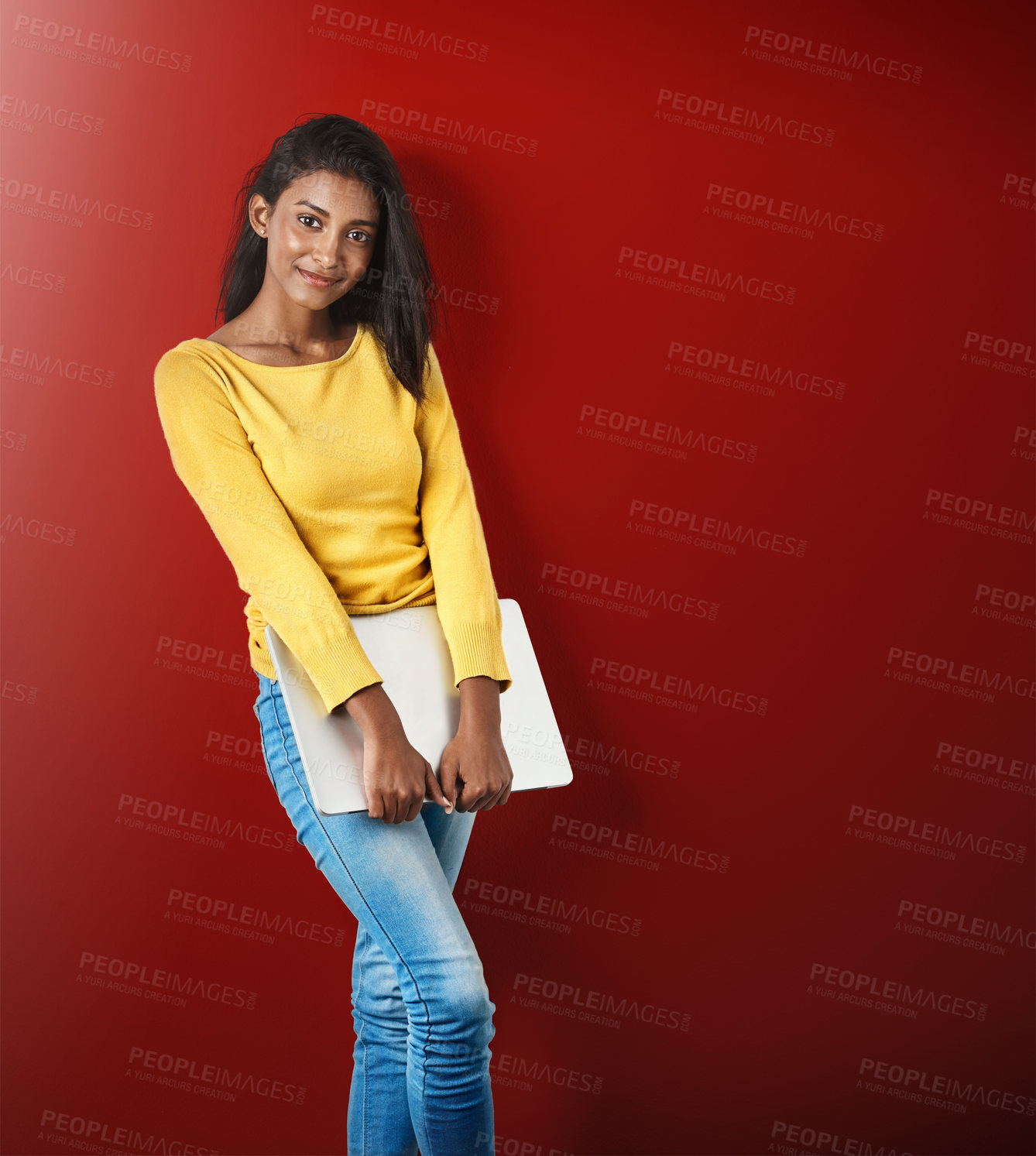 Buy stock photo Studio portrait of an attractive young woman holding a laptop against a red background