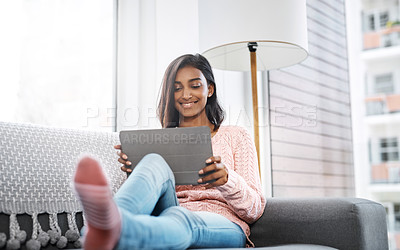 Buy stock photo Cropped shot of a beautiful young woman using a tablet while chilling on the sofa in the living room at home