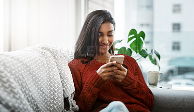 Buy stock photo Cropped shot of a beautiful young woman using a cellphone while chilling on the sofa in the living room at home