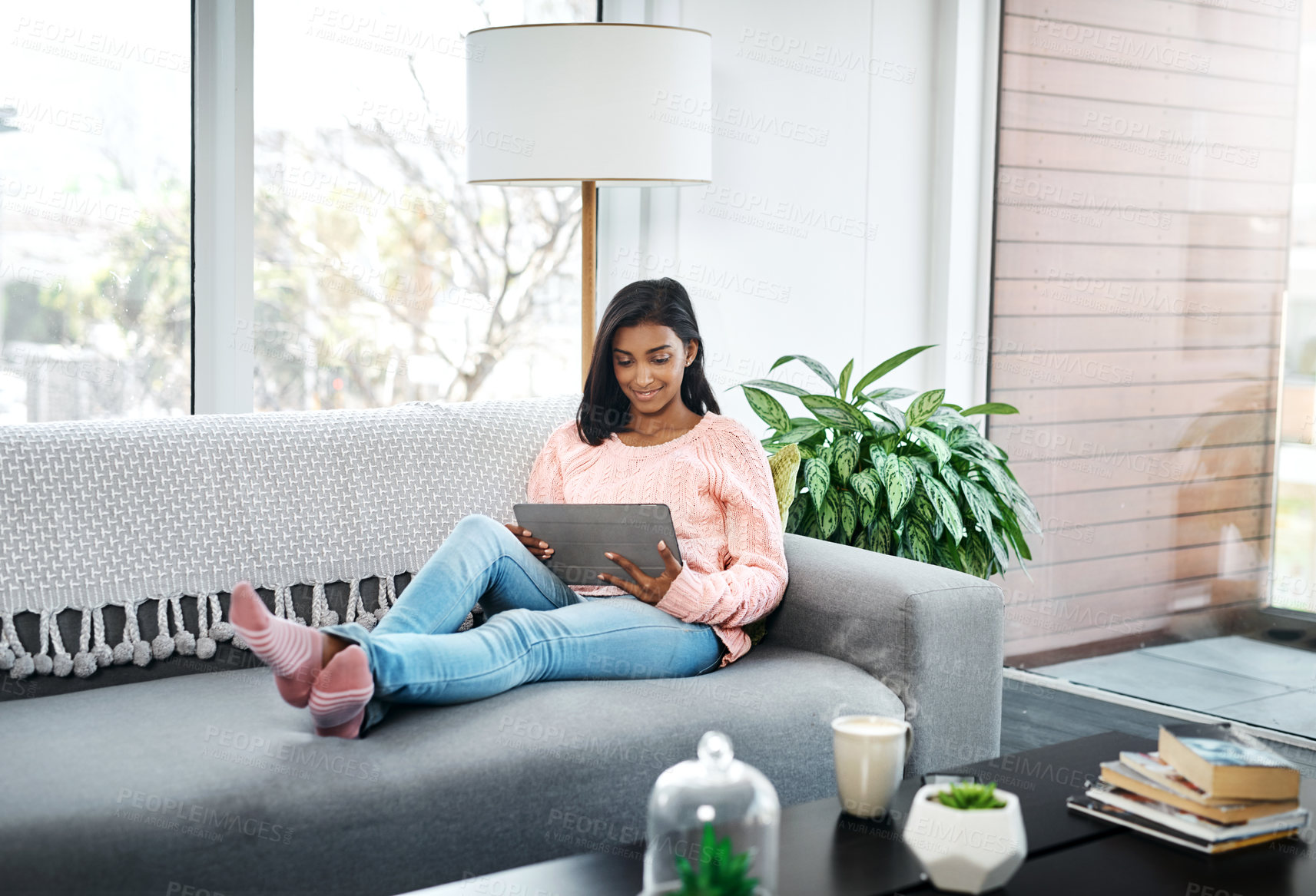 Buy stock photo Cropped shot of a beautiful young woman using a tablet while chilling on the sofa in the living room at home