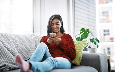 Buy stock photo Cropped shot of a beautiful young woman using a cellphone while chilling on the sofa in the living room at home