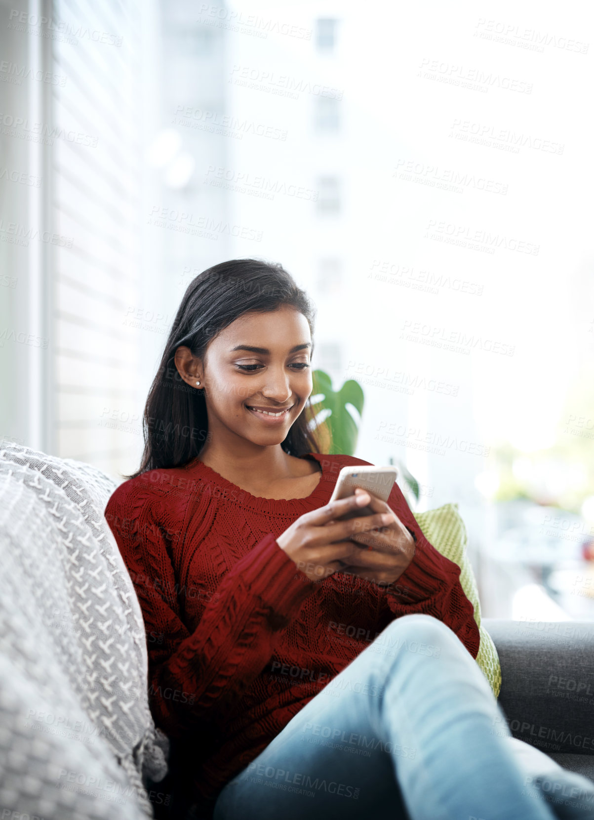 Buy stock photo Relax, home and Indian woman on couch with phone for social media, networking or reading on weekend. Happy, scroll and girl on sofa or smartphone for communication, online chat or smile in lounge