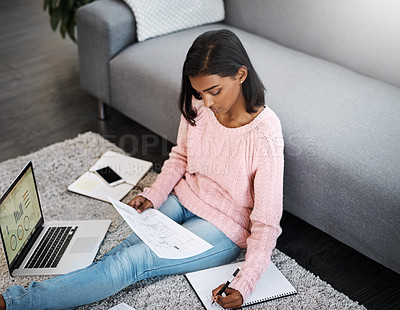Buy stock photo Shot of a young beautiful woman using a laptop and going through paperwork while sitting on the floor in the living room at home