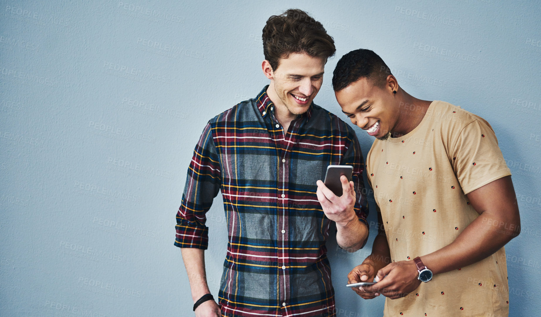 Buy stock photo Studio shot of two young men using a mobile phone together against a gray background