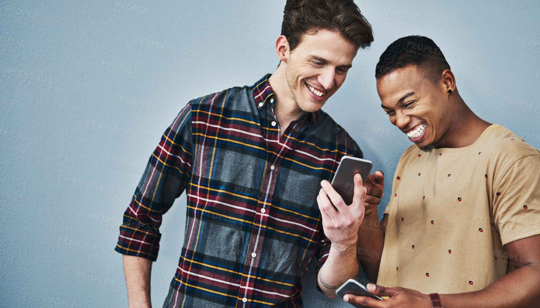 Buy stock photo Studio shot of two young men using a mobile phone together against a gray background