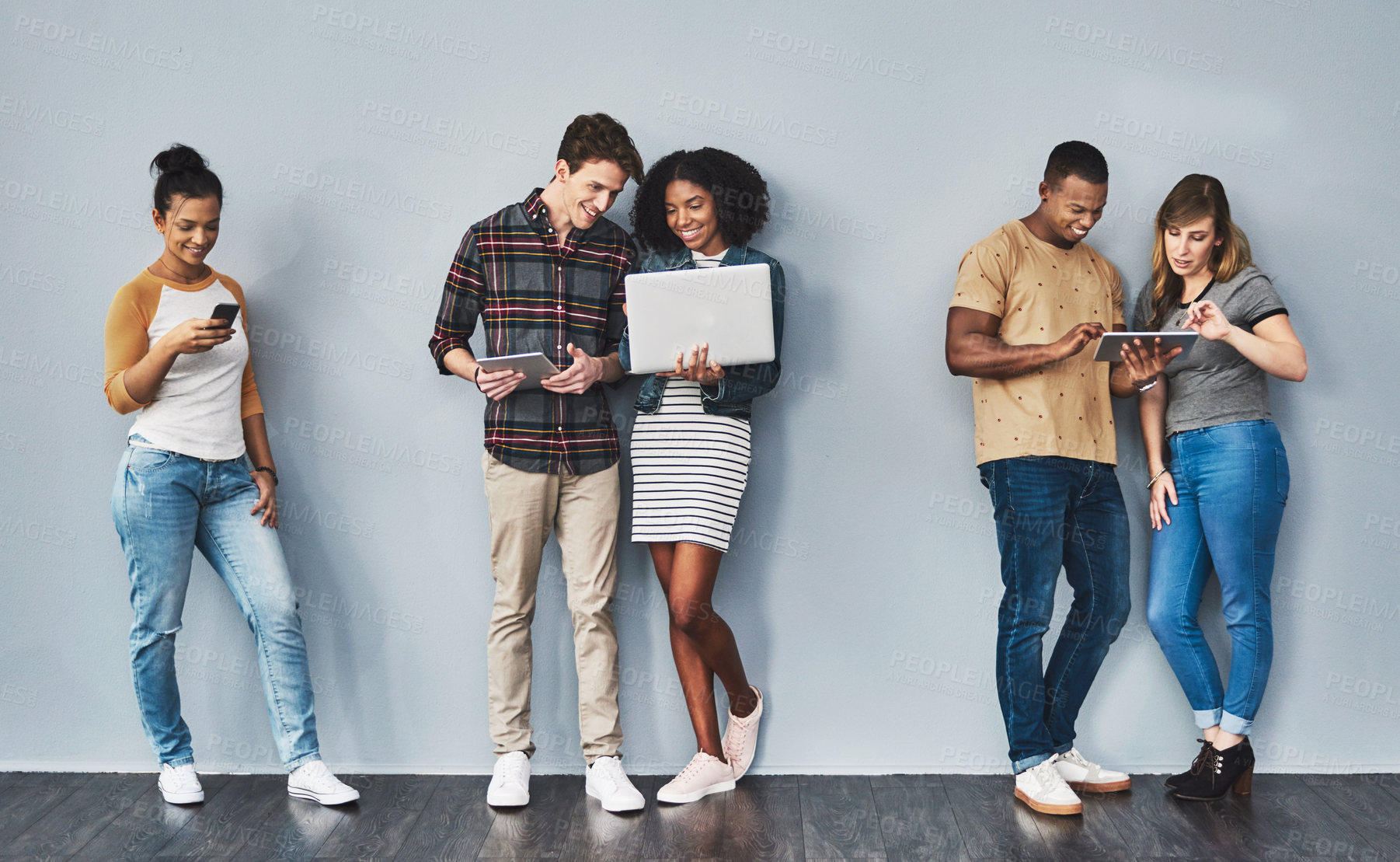 Buy stock photo Studio shot of a group of young people using wireless technology against a gray background