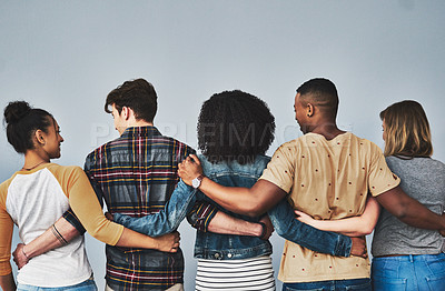 Buy stock photo Rearview studio shot of a diverse group of young people embracing each other against a gray background