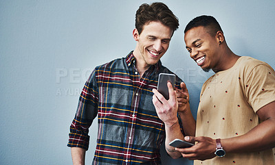 Buy stock photo Studio shot of two young men using a mobile phone together against a gray background