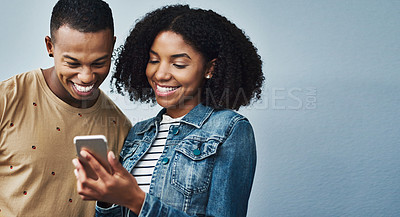 Buy stock photo Studio shot of a young man and woman using a mobile phone together against a gray background