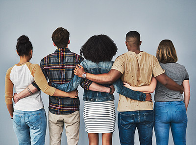 Buy stock photo Rearview studio shot of a diverse group of young people embracing each other against a gray background