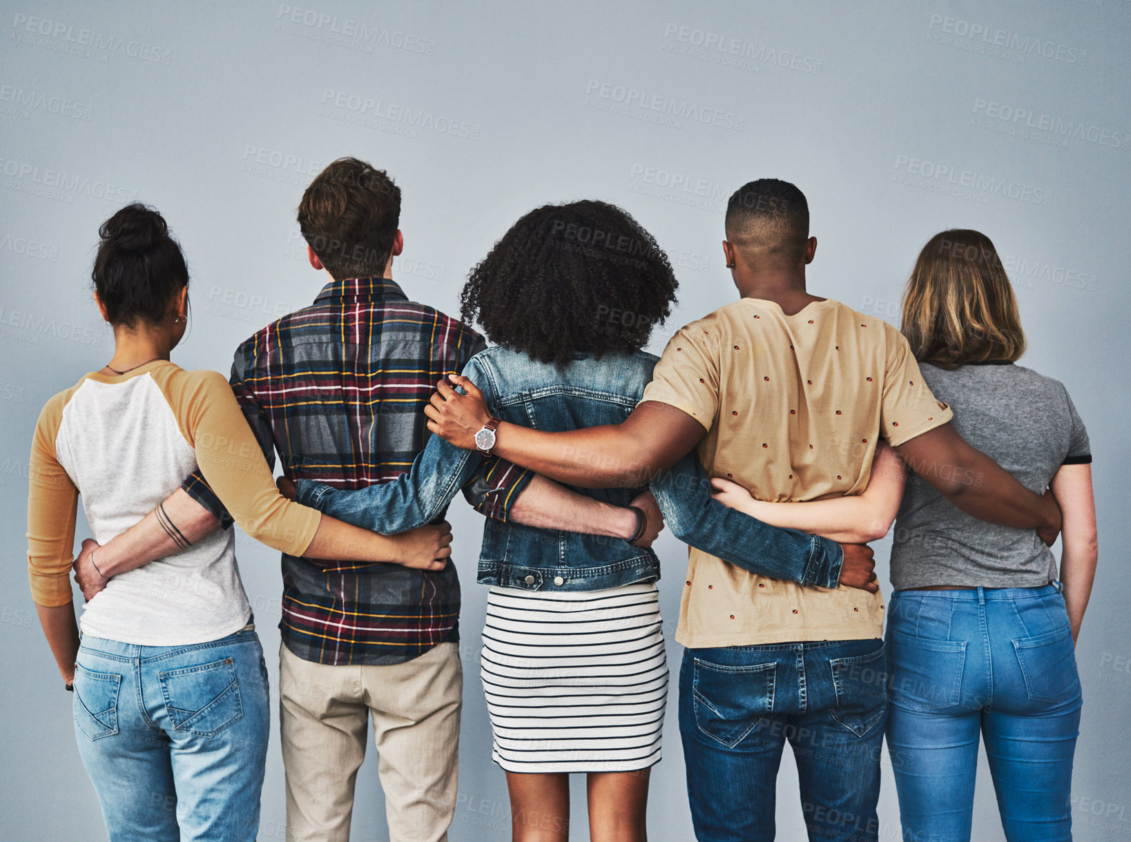 Buy stock photo Rearview studio shot of a diverse group of young people embracing each other against a gray background