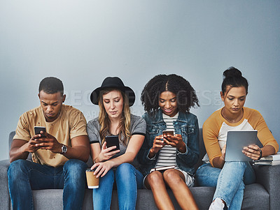 Buy stock photo Studio shot of young people sitting on a sofa and using wireless technology against a gray background