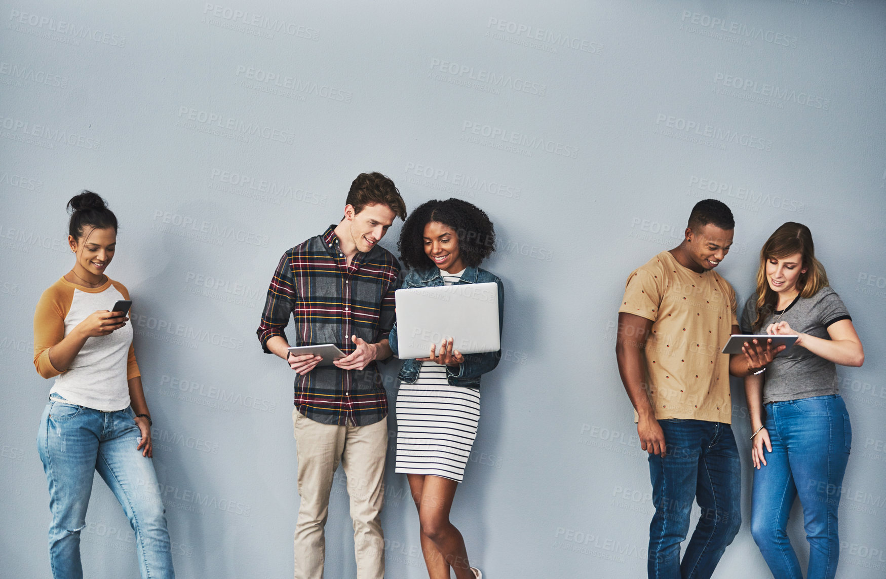 Buy stock photo Studio shot of a group of young people using wireless technology against a gray background