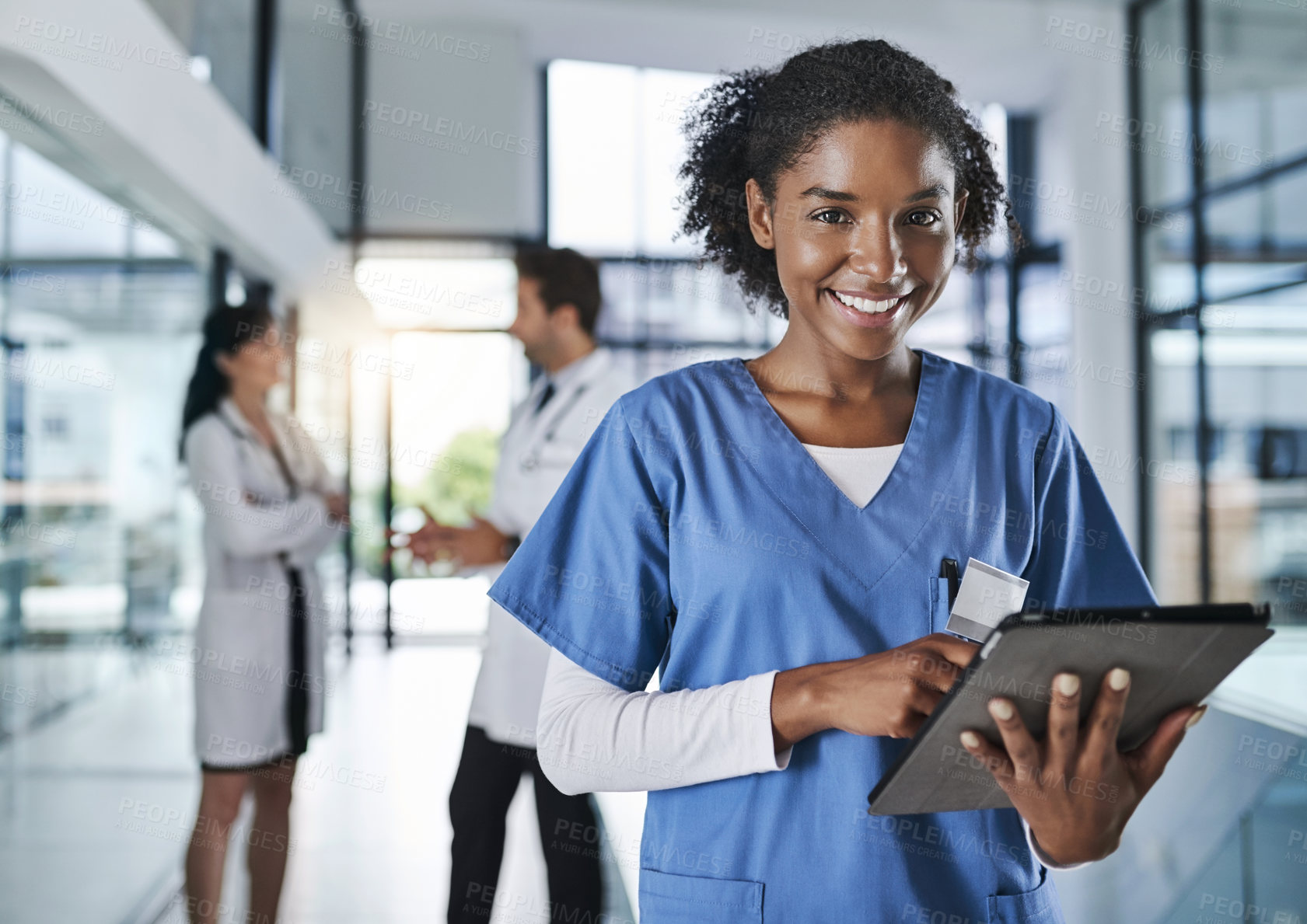 Buy stock photo Shot of a young doctor using a digital tablet in a hospital with her colleagues in the background