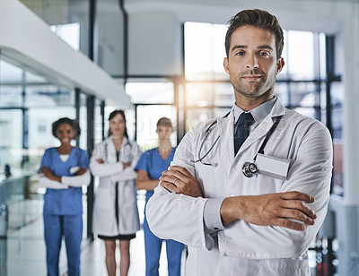 Buy stock photo Portrait of a confident young doctor working in a hospital with his colleagues in the background