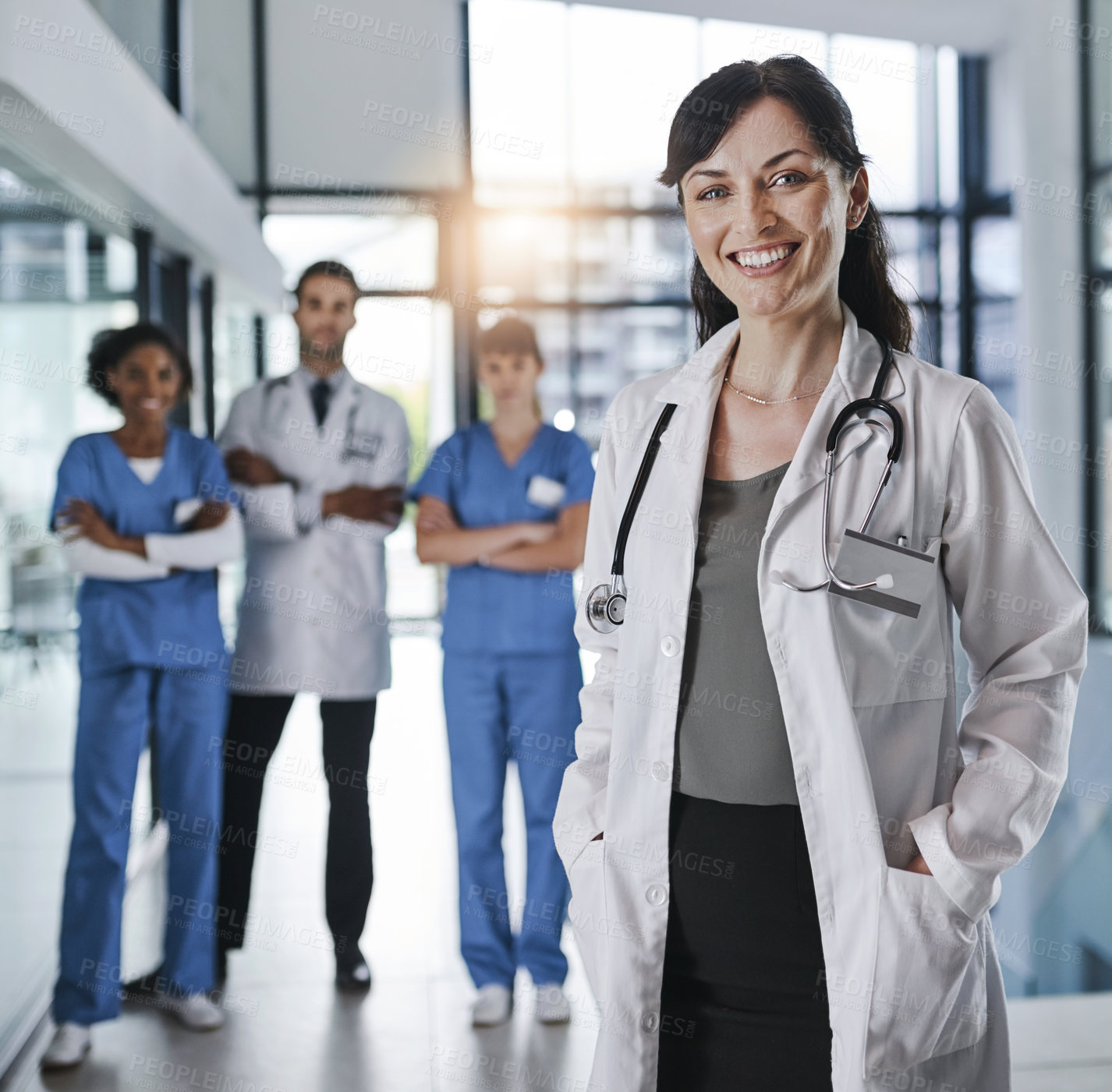 Buy stock photo Portrait of a confident mature doctor working in a hospital with her colleagues in the background