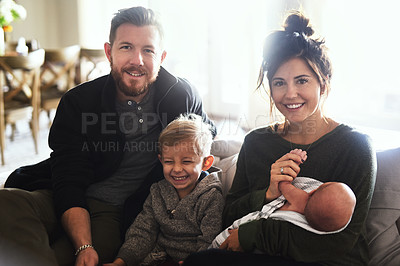 Buy stock photo Portrait of a cheerful young family seated on a sofa together at home during the day
