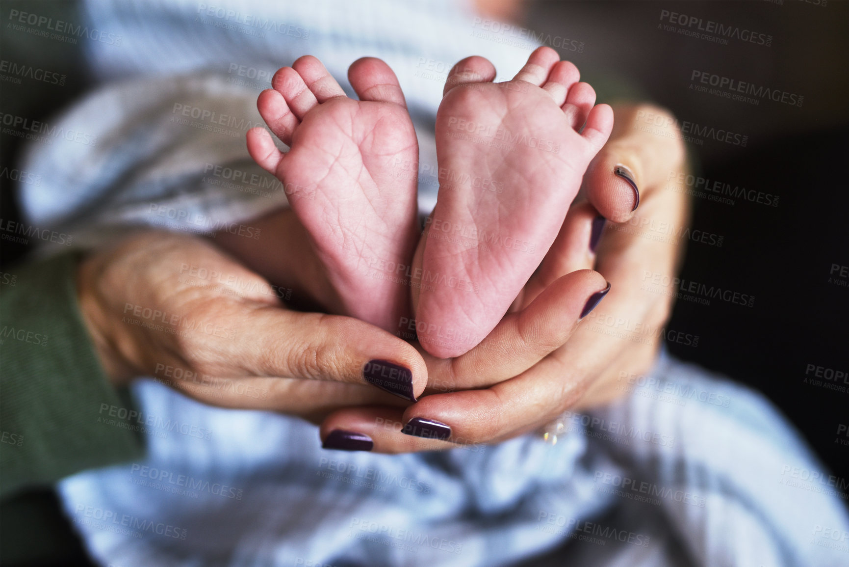 Buy stock photo Closeup of a unrecognizable woman holding her little infant child's tiny feet in her hands at home during the day