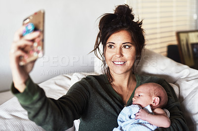 Buy stock photo Shot of a cheerful young woman lying on the sofa while holding her little infant son and taking a selfie at home during the day
