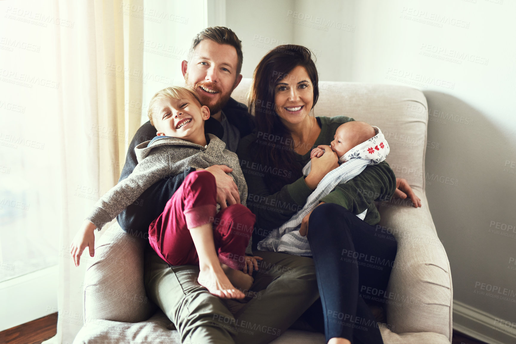 Buy stock photo Shot of a cheerful young family seated on a sofa together at home during the day