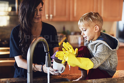 Buy stock photo Shot of a cheerful little boy wearing yellow washing gloves helping his mother do dishes in the kitchen at home