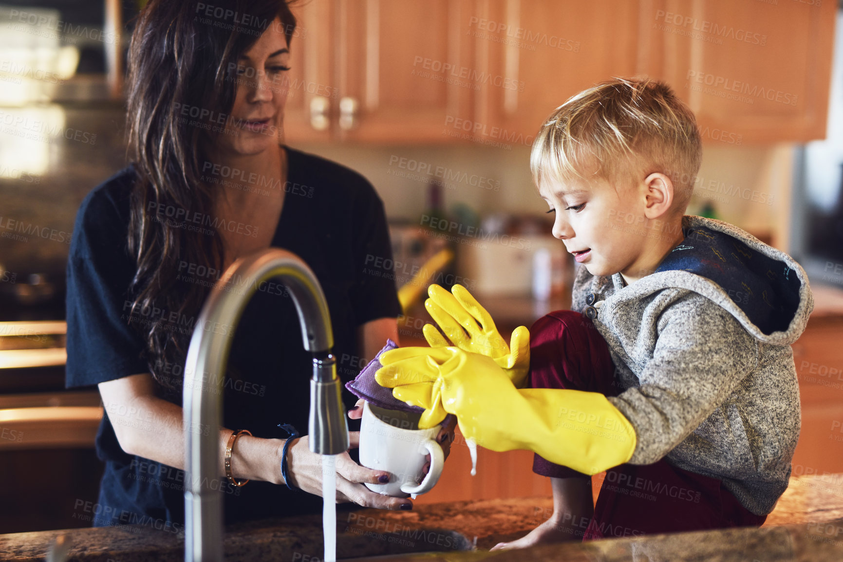 Buy stock photo Shot of a cheerful little boy wearing yellow washing gloves helping his mother do dishes in the kitchen at home