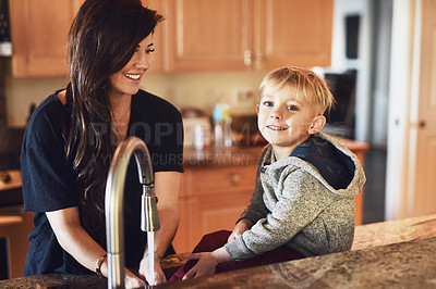 Buy stock photo Shot of a cheerful young woman washing her hands while her little boy sits next to her and contemplates at home during the day