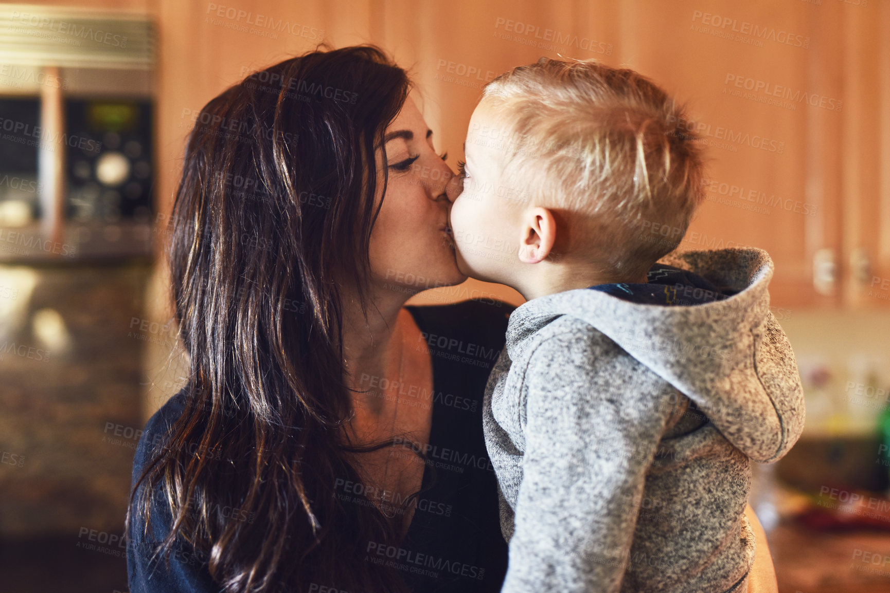 Buy stock photo Shot of a cheerful little boy giving his mother a little kiss at home during the day