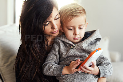 Buy stock photo Shot of a carefree young woman browsing on a cellphone with her little boy while being seated on a sofa at home during the day