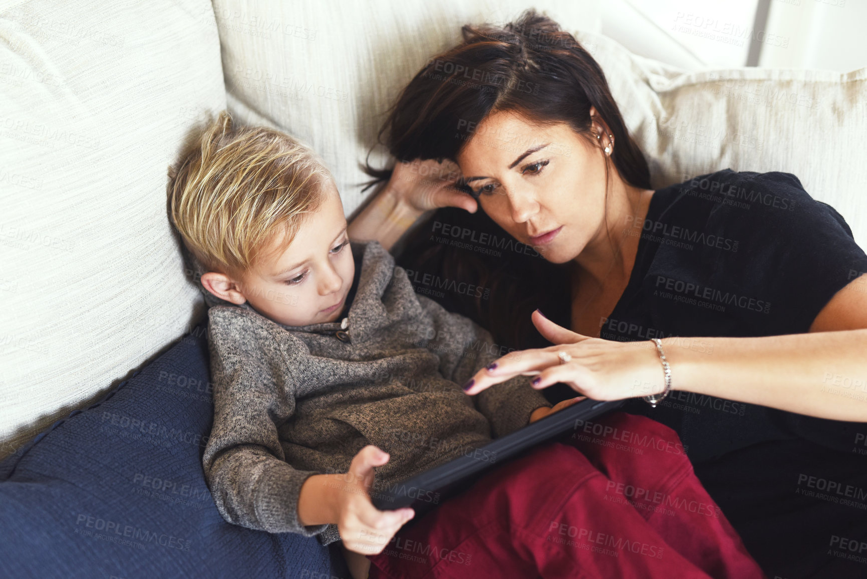 Buy stock photo Shot of a carefree young woman browsing on a digital tablet with her little boy while being seated on a sofa at home during the day