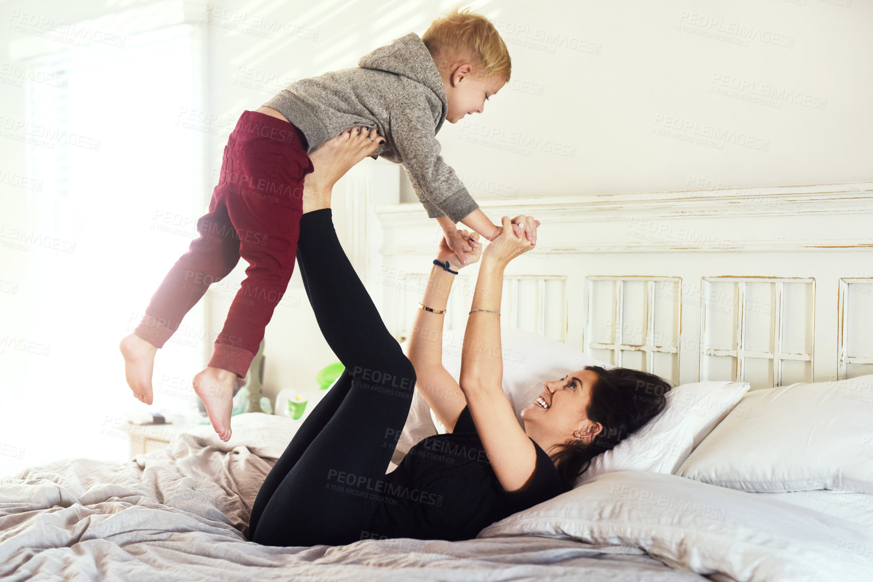 Buy stock photo Shot of a cheerful little boy being lifted up in the air by his mother's legs in the bedroom at home during the day