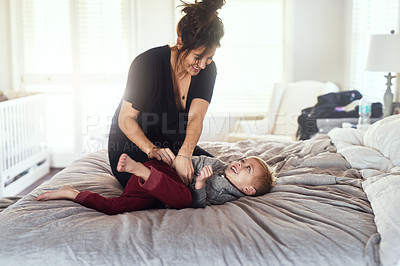 Buy stock photo Shot of a cheerful little boy being tickled by his mother while they both hang out on the bed at home during the day