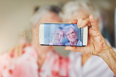 Buy stock photo Shot of two happy elderly women taking selfies together on a mobile phone