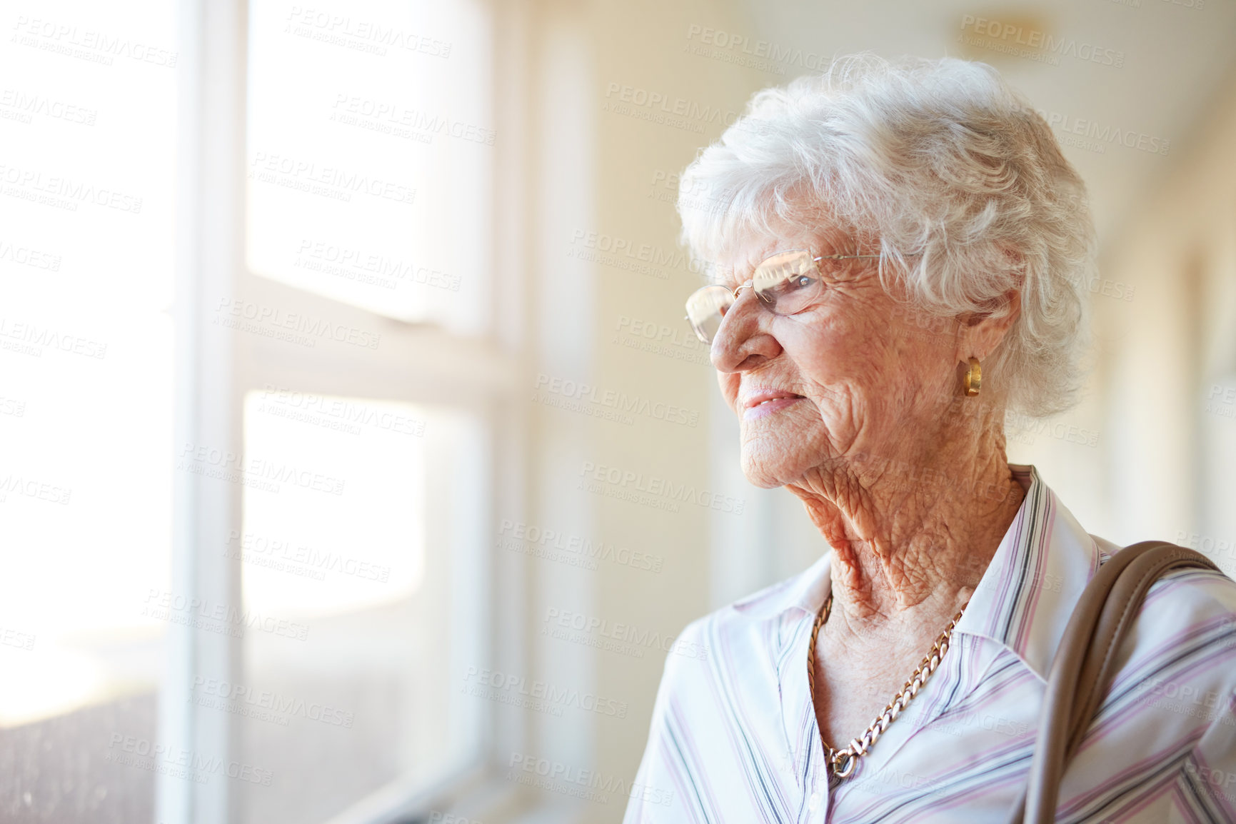Buy stock photo Shot of an elderly woman looking out of the window before she leaves home