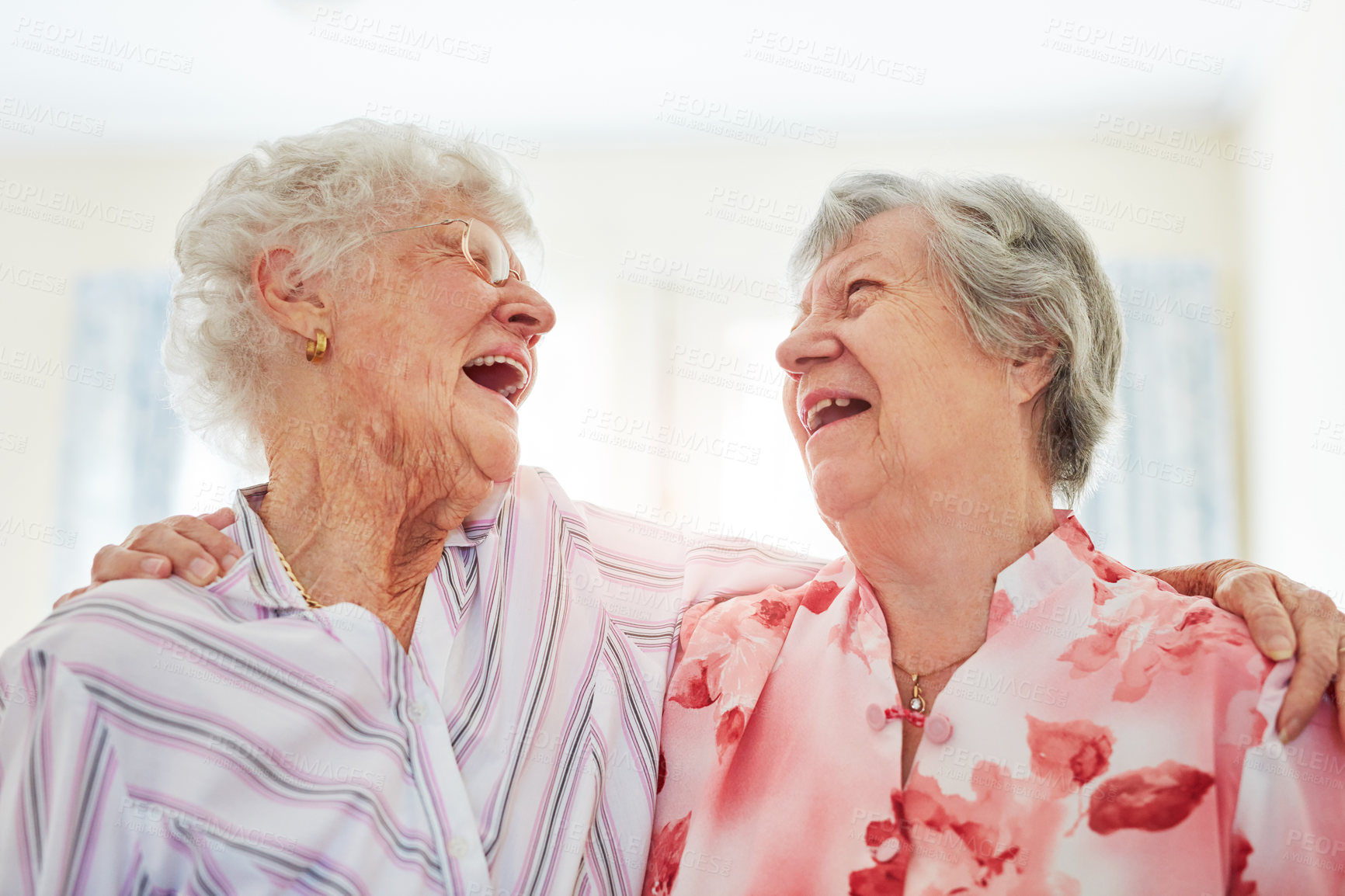 Buy stock photo Shot of two happy elderly women embracing each other at home