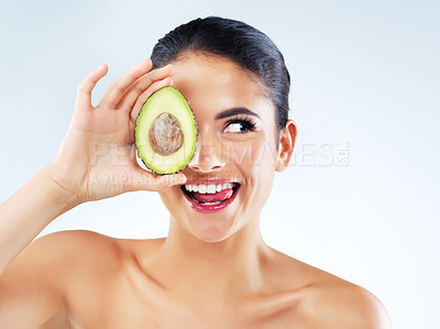 Buy stock photo Studio shot of an attractive young woman covering her eye with an avocado against a gray background