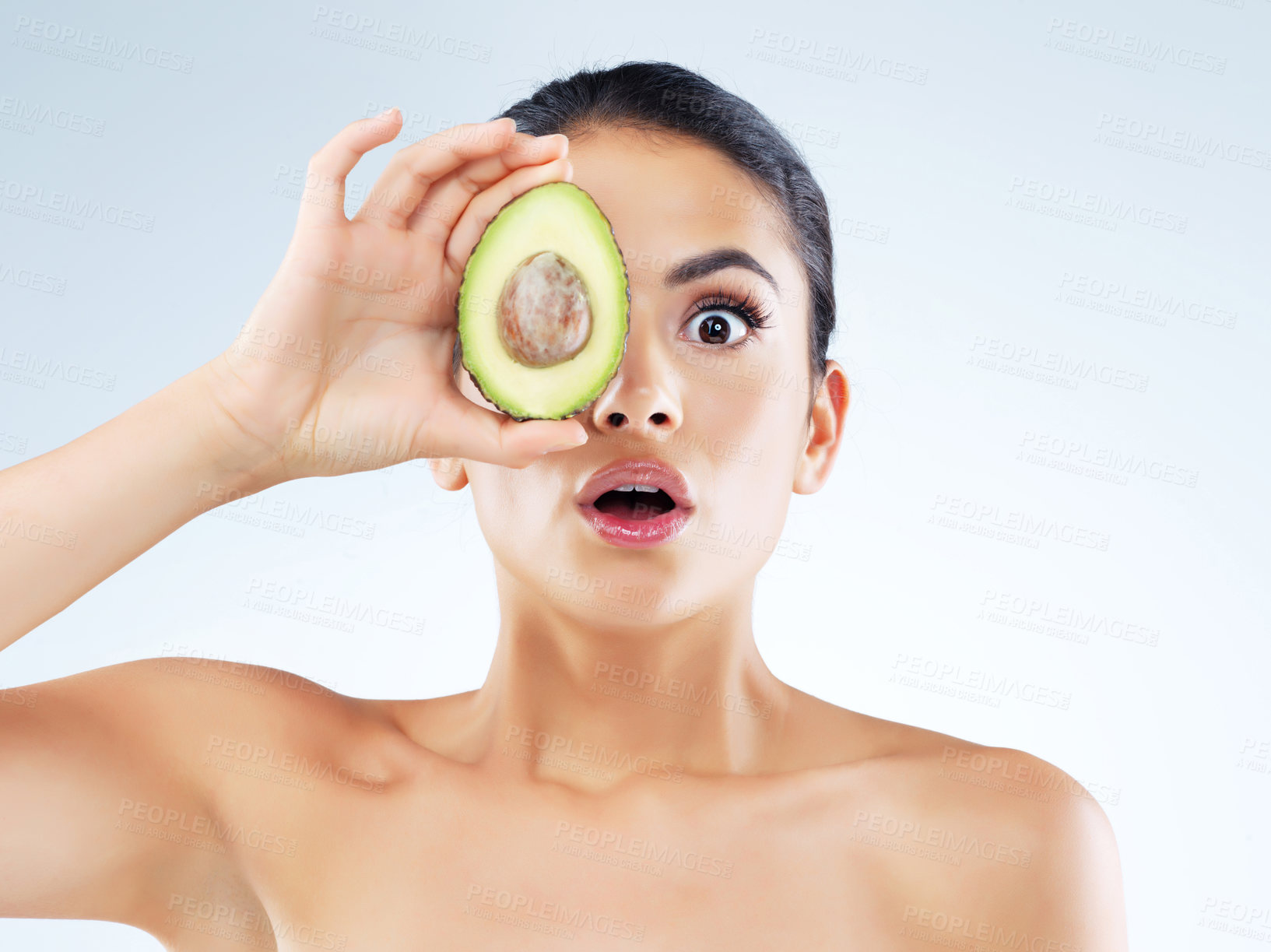 Buy stock photo Studio portrait of an attractive young woman covering her eye with an avocado against a gray background