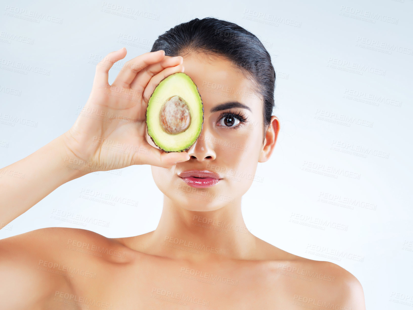 Buy stock photo Studio portrait of an attractive young woman covering her eye with an avocado against a gray background