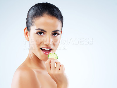 Buy stock photo Studio portrait of an attractive young woman eating a slice of cucumber against a gray background