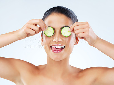 Buy stock photo Studio portrait of an attractive young woman covering her eyes with cucumbers against a gray background