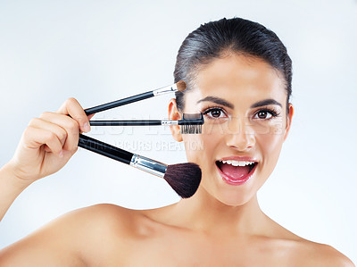 Buy stock photo Studio portrait of an attractive young woman holding makeup brushes against a gray background